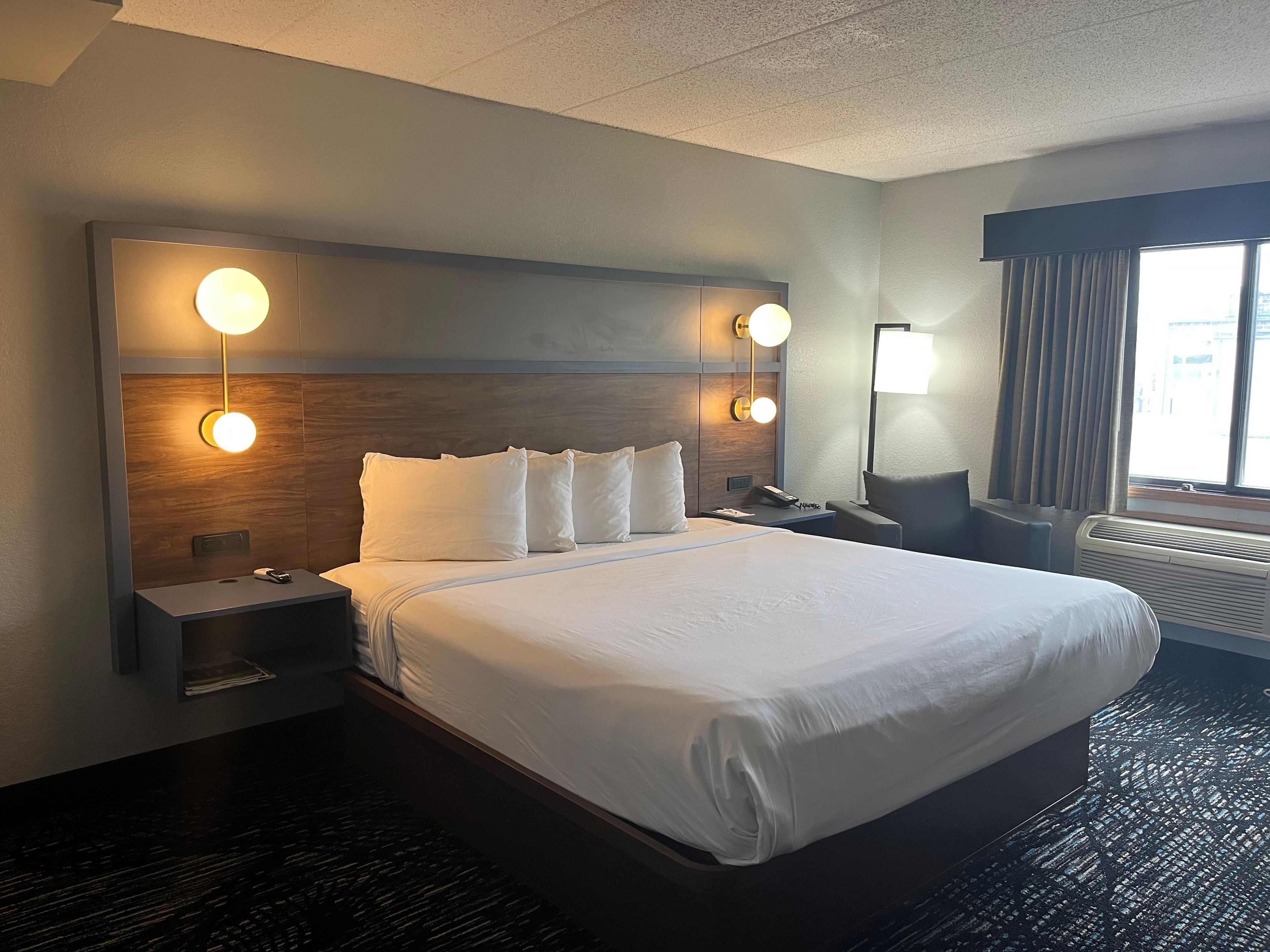 A hotel room with a large bed, two bedside tables, a nightstand, a lamp, and a window with curtains.