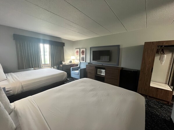 A hotel room with two beds, a desk with a chair, a television, and a microwave.