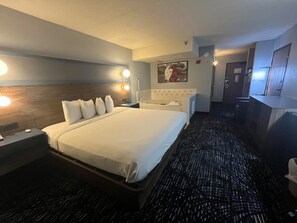 A hotel room with a large bed, bedside lamps, a headboard, a bathroom with a bathtub, and a mirror. - AmericInn by Wyndham Lincoln North (Lincoln)