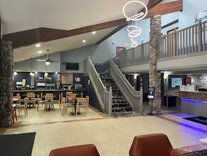 Un restaurante con bar, varias zonas de estar y una escalera que conduce a un nivel superior.