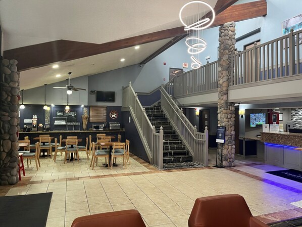 A restaurant with a bar, multiple seating areas, and a staircase leading to an upper level. - AmericInn by Wyndham Lincoln North (Lincoln)