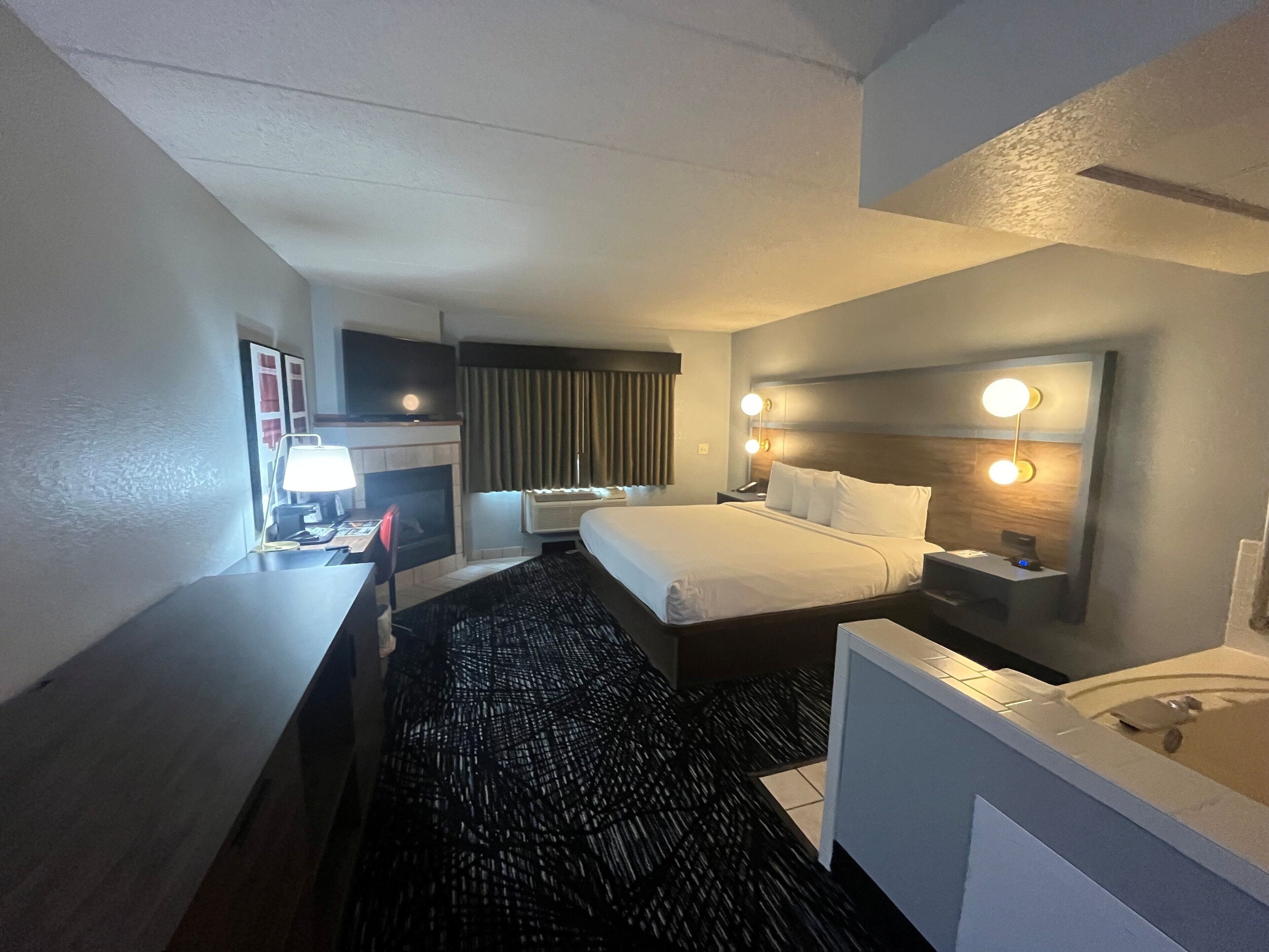 Una habitación de hotel con cama, escritorio, silla y baño con bañera.