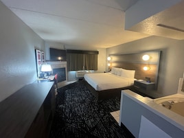 A hotel room with a bed, desk, chair, and a bathroom with a bathtub.
