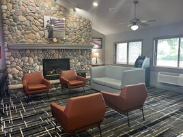 Una habitación con pared de piedra, chimenea, sofá, dos sillones y un cajero automático.