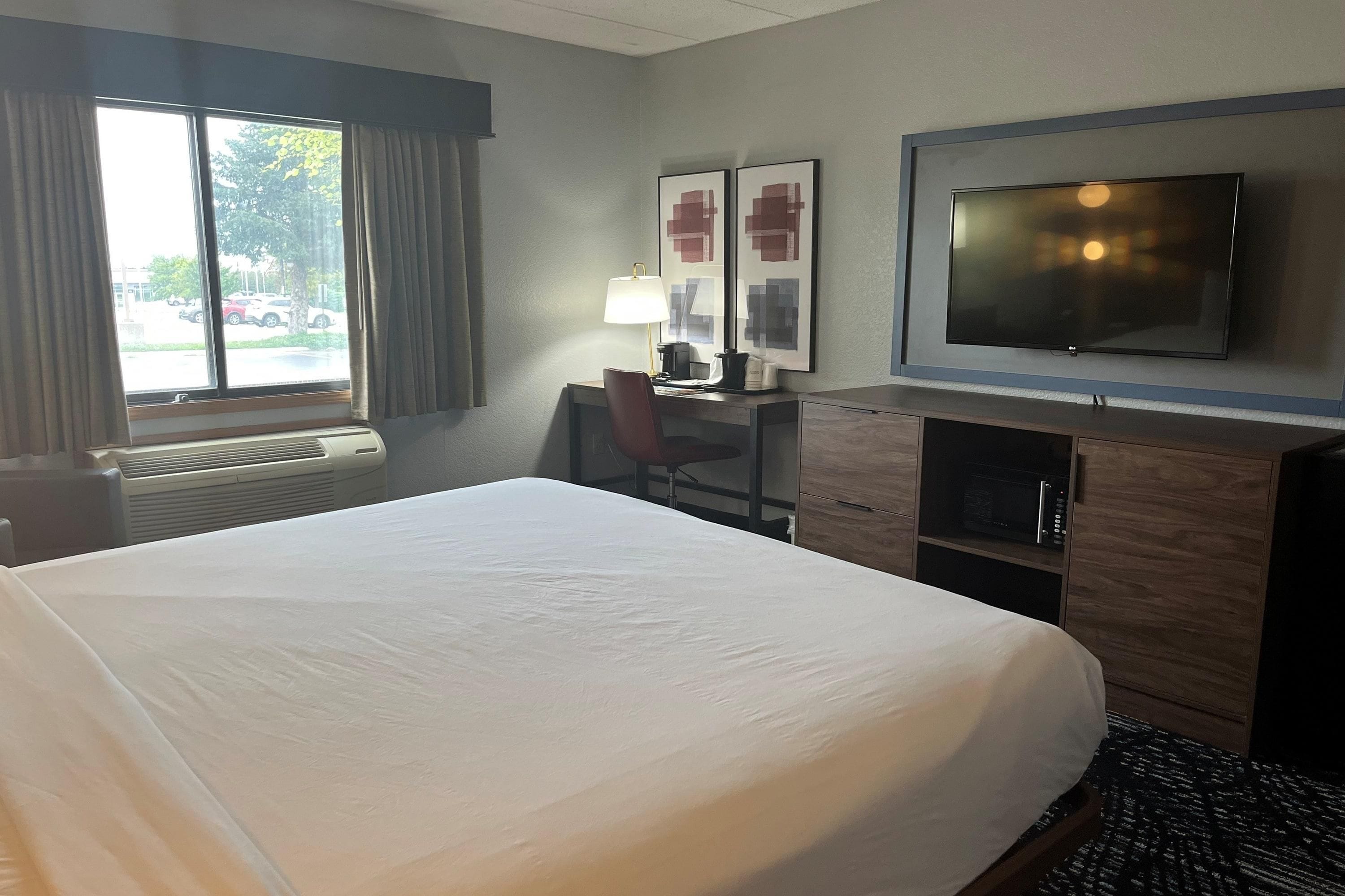 Habitación de hotel con cama, escritorio, silla, televisor y ventana con cortinas.