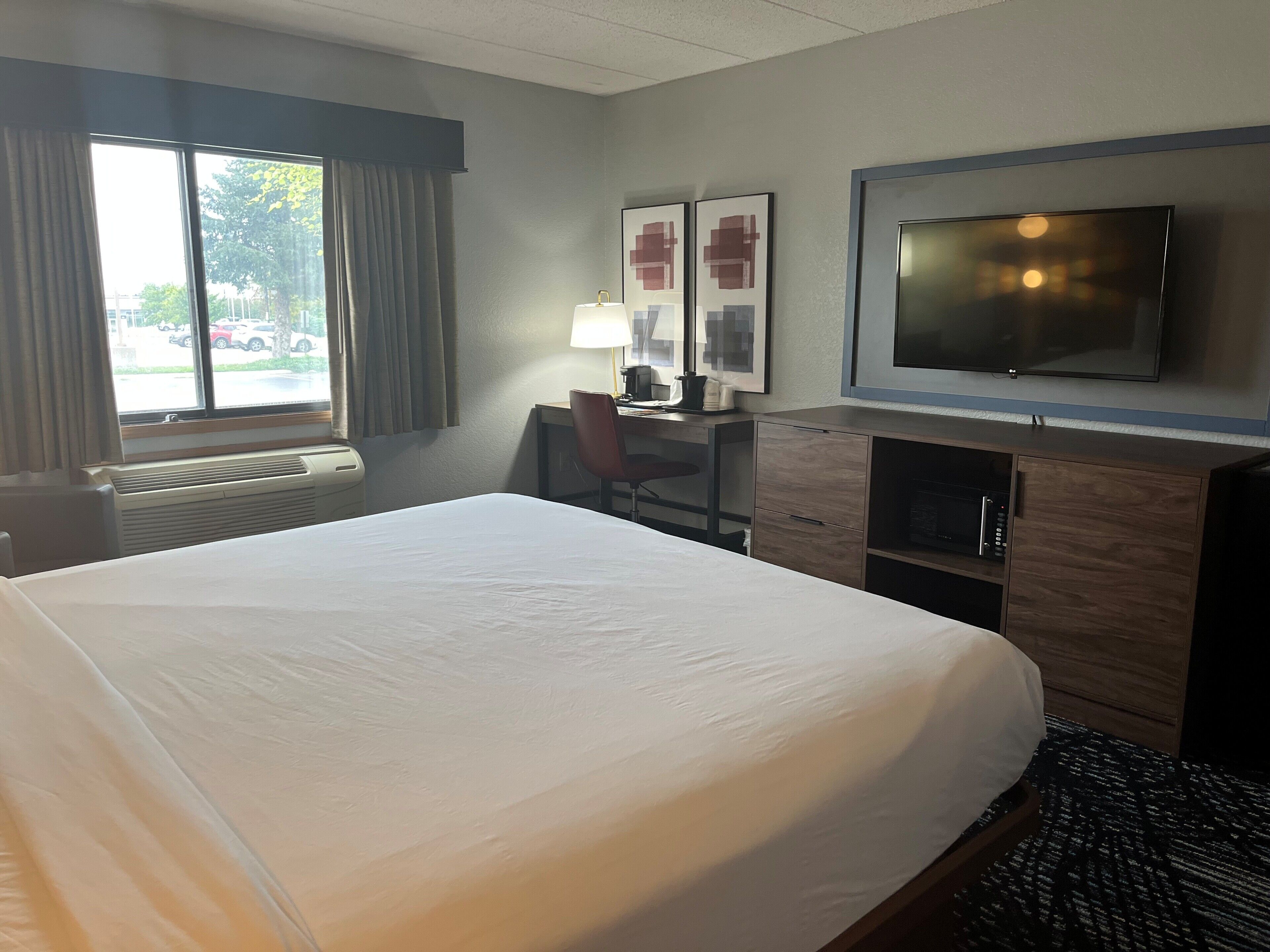 Habitación de hotel con una cama grande, un escritorio con silla, televisión y ventana con cortinas.