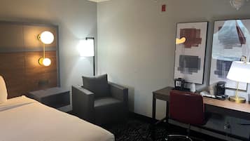 A hotel room with a bed, a desk, a chair, a lamp, and a wall-mounted mirror.