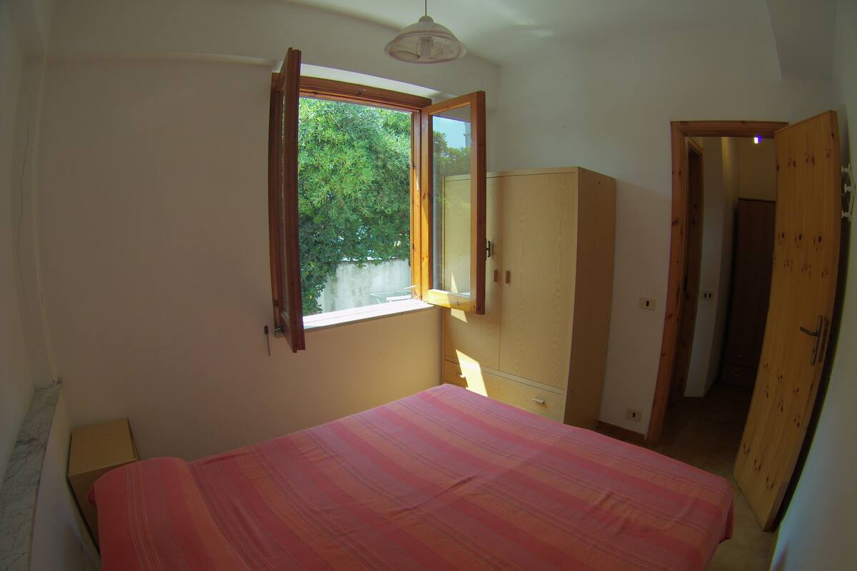 Quarto com cama, armário e janela com persiana aberta.