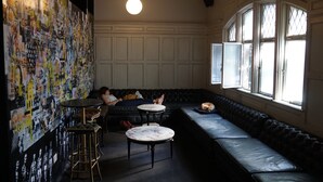 A cozy lounge area with a black leather sofa, a round table, and a wall covered with colorful artwork. - Art Factory Beer Garden - Hostel (Buenos Aires)