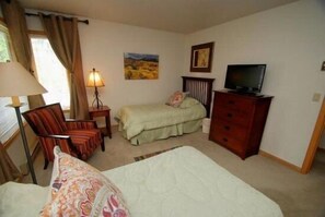 Une chambre d’hôtel comprenant un lit, une chaise, un bureau, une commode, un téléviseur et une fenêtre avec des rideaux.