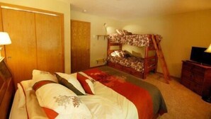 Een slaapkamer met een stapelbed, een nachtkastje, een lamp en een dressoir.