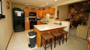 A kitchen with wooden cabinets, a black refrigerator, a central island with stools, and a stone wall. - Snowdance Manor 2 Bedroom Holiday home by Key to the Rockies (Keystone)