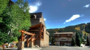 A lodge with a wooden entrance, a stone base, and a mountain backdrop. - Snowdance Manor 2 Bedroom Holiday home by Key to the Rockies (Keystone)