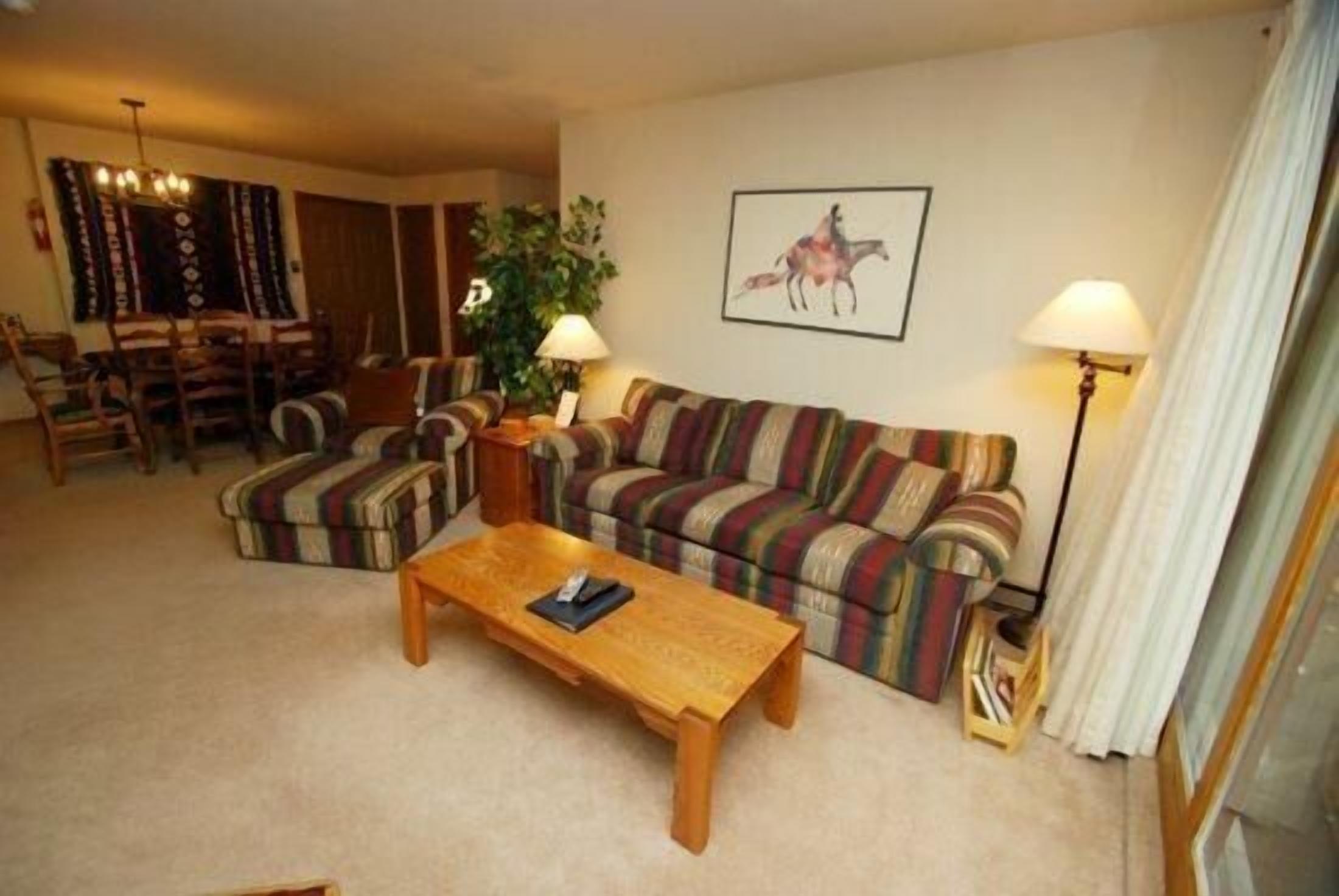 Una sala de estar acogedora con un sofá a rayas, una mesa de centro de madera y un comedor con sillas y una mesa.