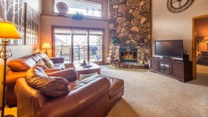 A living room with a stone fireplace, leather sofa, and a television. - Snowdance Manor 2 Bedroom Holiday home by Key to the Rockies (Keystone)