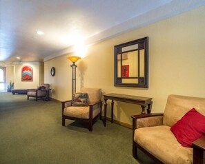 A carpeted hallway with a sofa, a chair, a lamp, and a mirror on the wall.