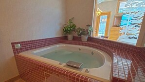 A bathroom with a freestanding bathtub, red tiled walls, a small potted plant, and a window with a view of a snowy landscape. - River Bank Lodge 1 Bedroom Apartment by Key to the Rockies (Keystone)