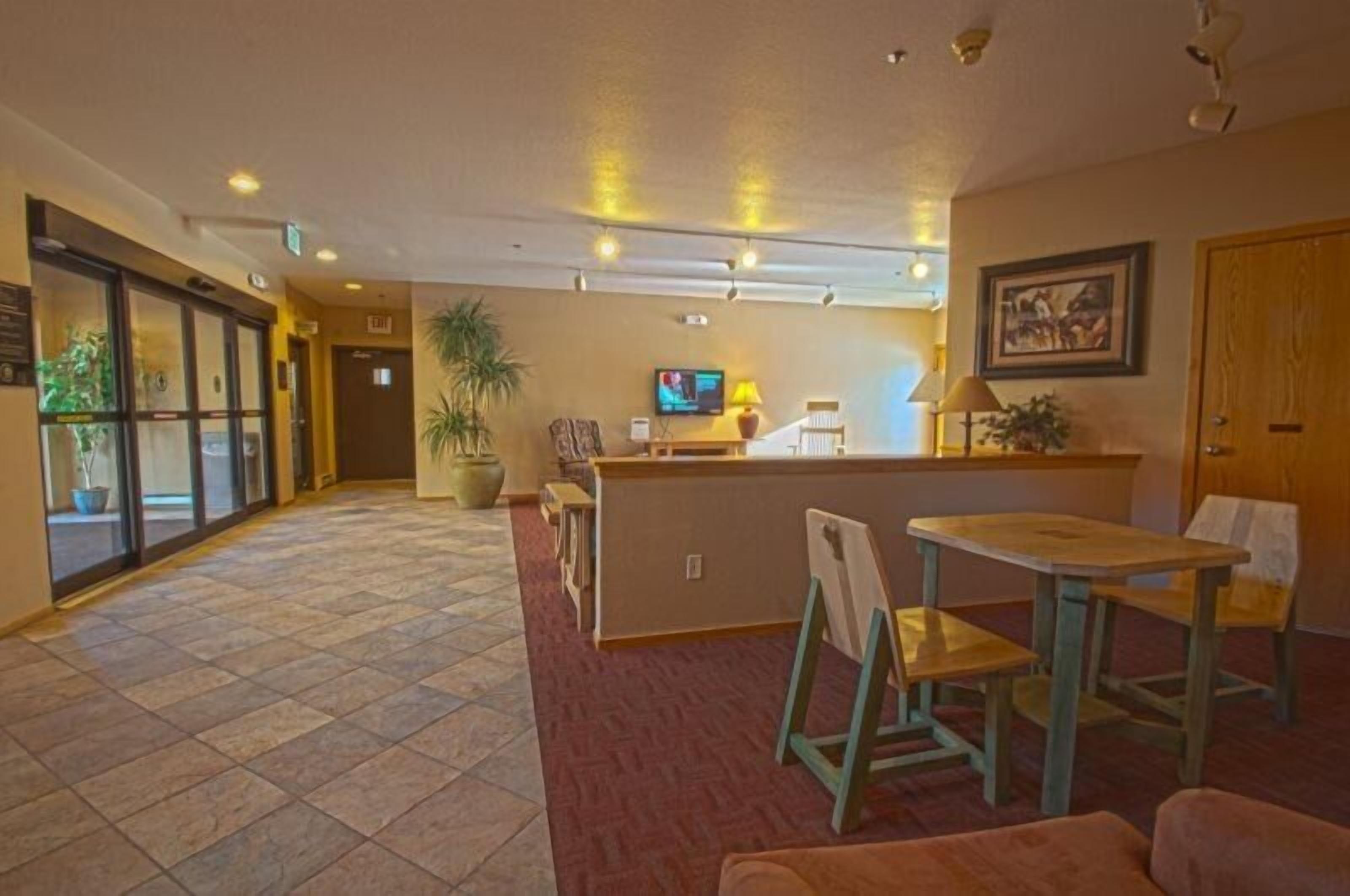 Un hall d’entrée avec un comptoir de réception, un téléviseur, une plante en pot et un espace détente comprenant une table et des chaises.