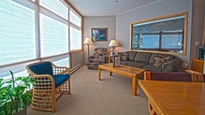 A cozy living room with a large window, a blue chair, a wooden coffee table, and a gray sofa. - River Bank Lodge 1 Bedroom Apartment by Key to the Rockies (Keystone)