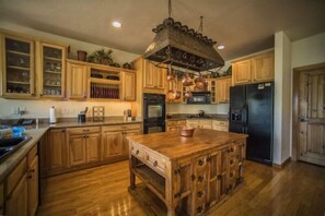 A kitchen with wooden cabinets, a central island, and a hanging pot rack. - Retreat at Summerwood 5 Bedroom Apartment by Key to the Rockies (Dillon)