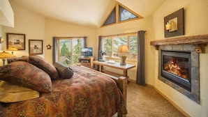 A cozy bedroom with a large bed, a fireplace, a desk, and a TV. - Retreat at Summerwood 5 Bedroom Apartment by Key to the Rockies (Dillon)