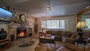 A cozy living room with a stone fireplace, leather furniture, a television, and a large window.