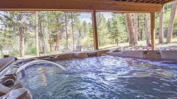 A hot tub with a wooden deck and a view of a forest.