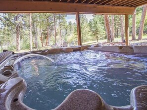 Un bain à remous avec une terrasse en bois et vue sur une forêt.