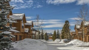 A snow-covered street with wooden buildings, a car, and a mountain in the background. - Snake River Village 3 Bedroom Apartment by Key to the Rockies (Keystone)