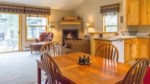 A cozy living room with a fireplace, a dining table, and a kitchen area with wooden cabinets. - Snake River Village 3 Bedroom Apartment by Key to the Rockies (Keystone)