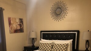Un letto rifatto con cura, con una coperta a motivi, due comodini con lampade, uno specchio decorativo a parete e un tappeto sul pavimento.