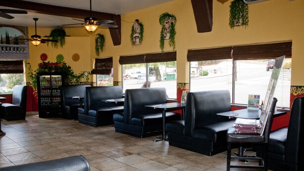 Interno di un ristorante con cabine, tavoli, ventilatori a soffitto e piante ornamentali.