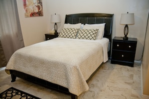 A neatly made bed with patterned bedding, two bedside tables with lamps, and a decorative wall piece.