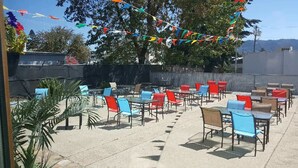 Una terrazza esterna con tavoli e sedie disposti in file, circondata da un muretto e alberi.