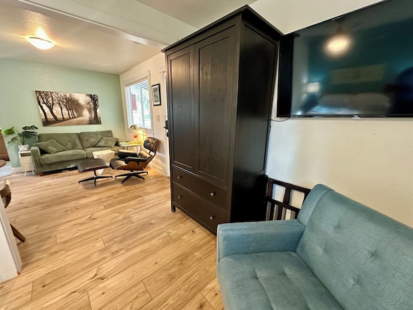 Un salón con un sofá azul, un sofá verde, piso de madera, un armario de madera oscura y un televisor de pantalla plana montado en la pared.