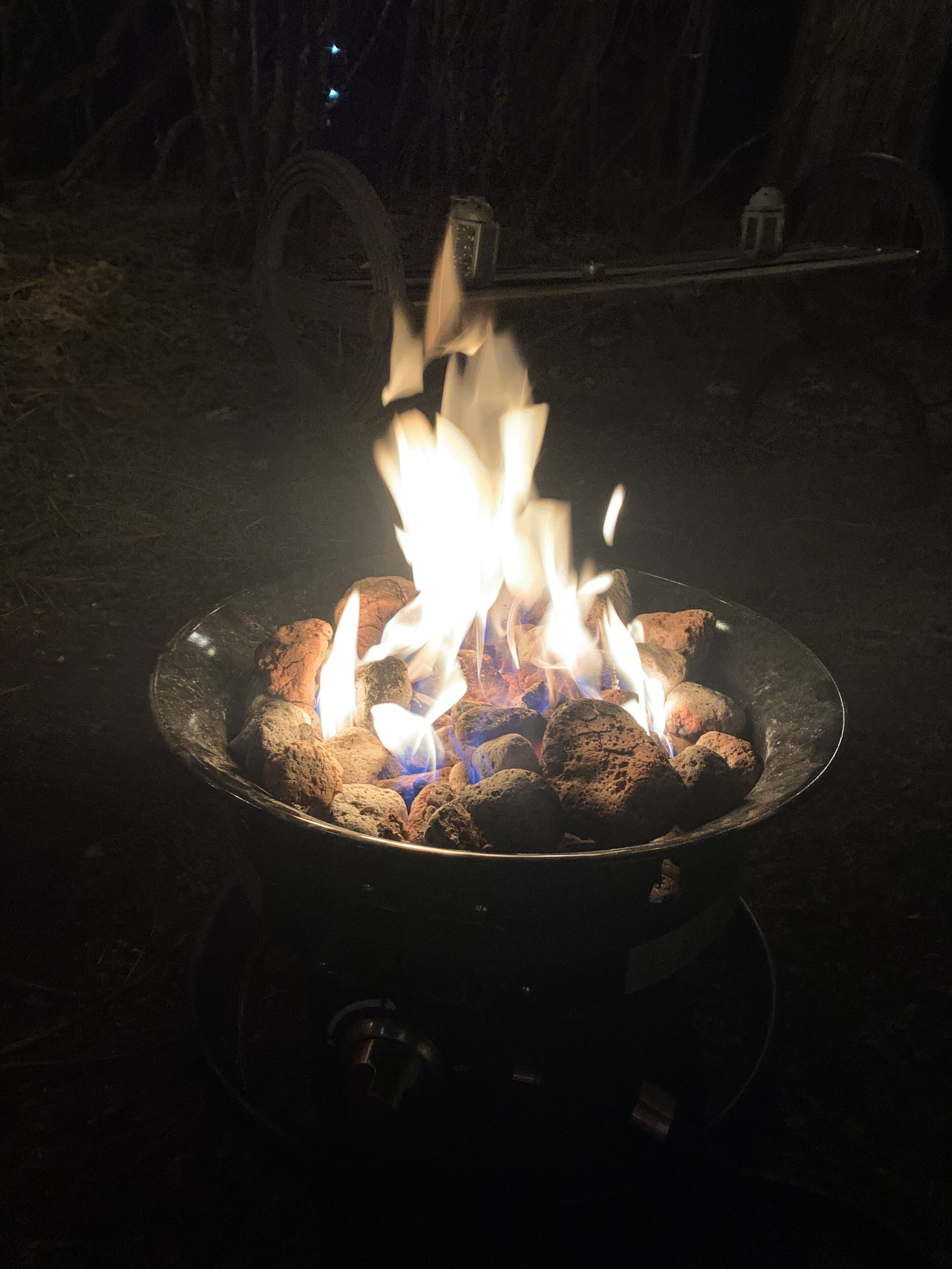 A campfire with logs and flames, surrounded by a metal fire pit.