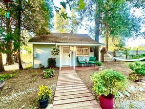 A small house with a porch, a wooden pathway leading to the entrance, and a fenced backyard. - The Pines Inn and Cottages (Grass Valley)