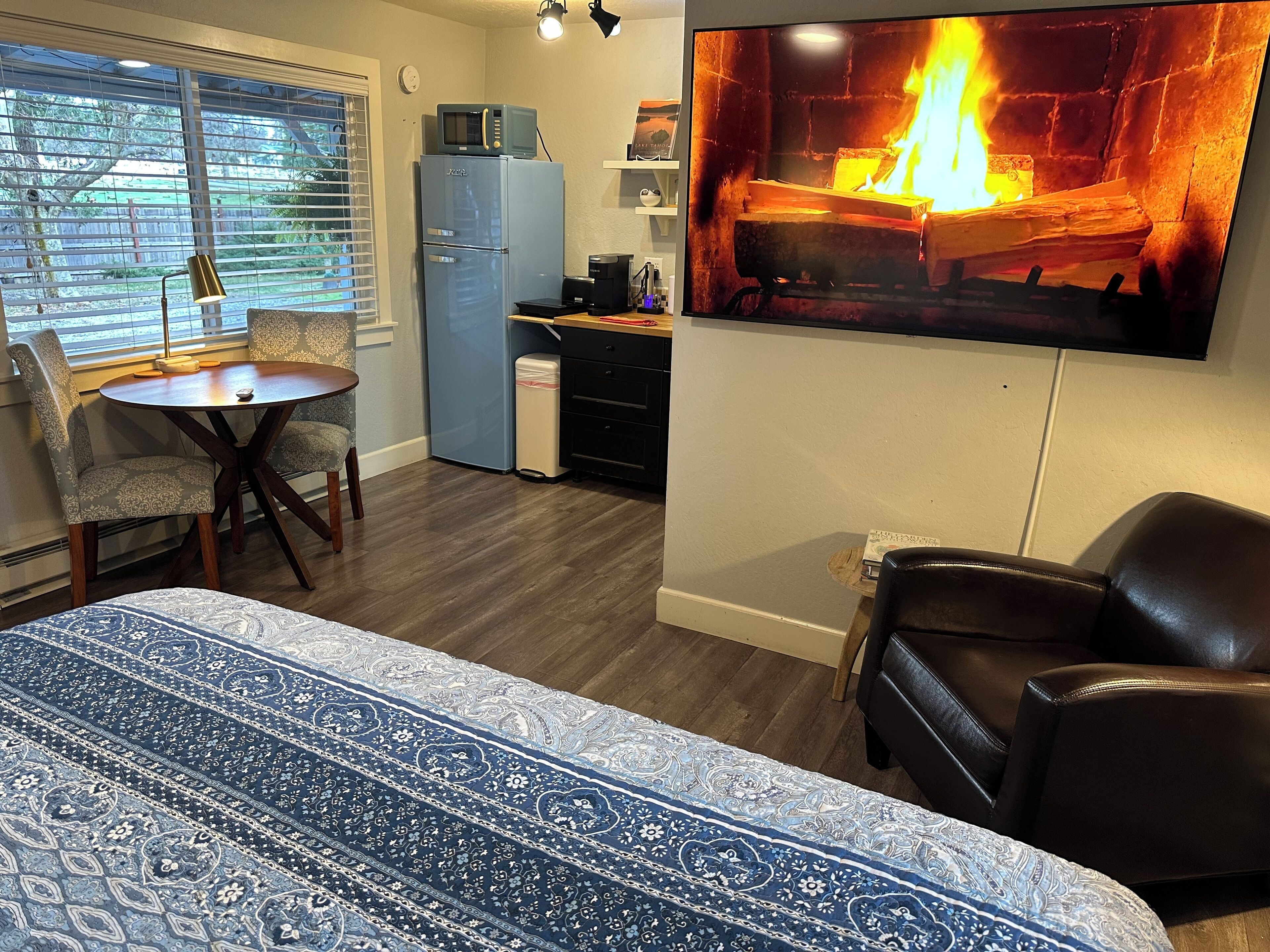 A cozy room with a bed, a dining table with chairs, a small kitchenette, and a fireplace.