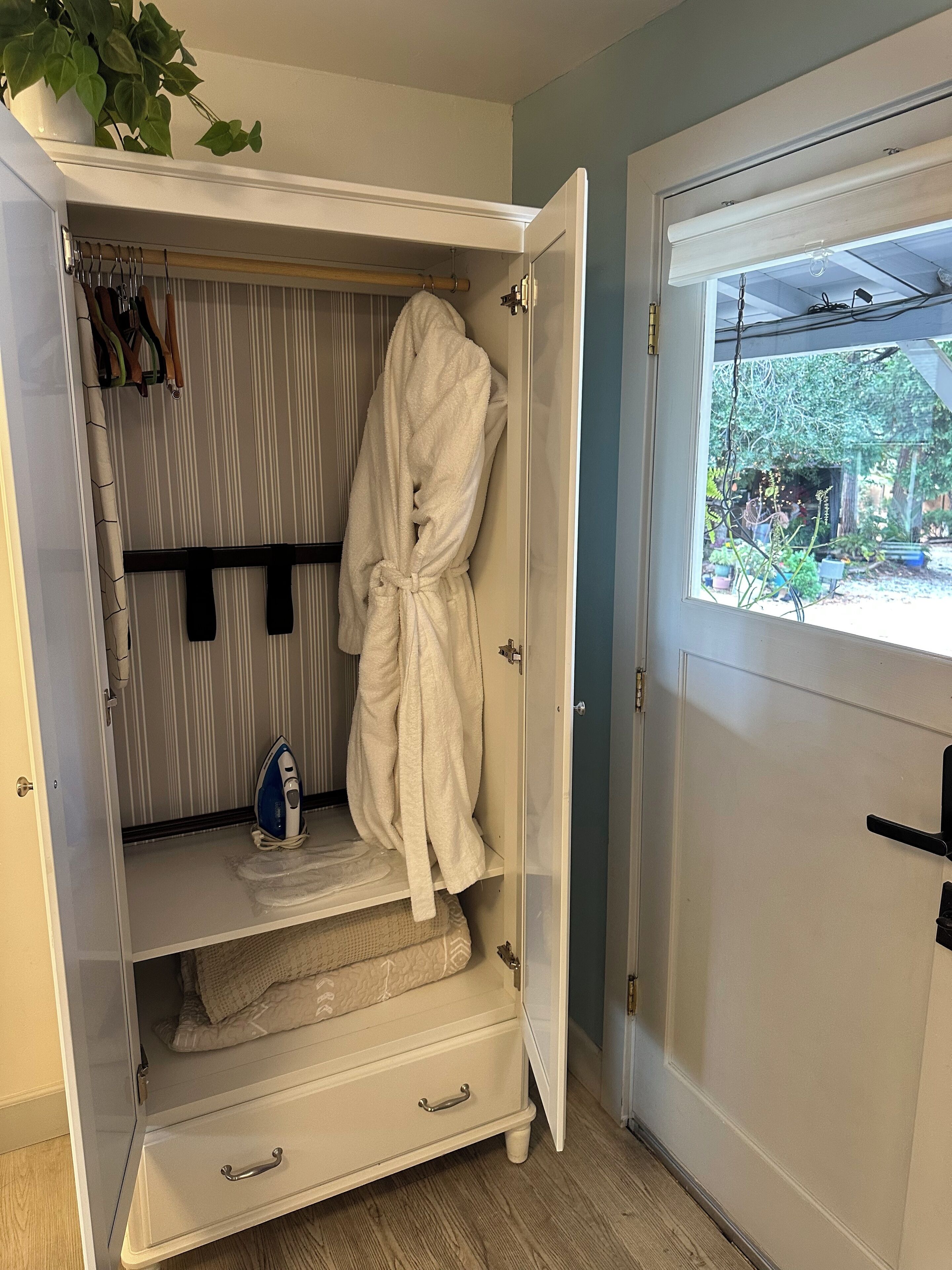 Un dressing où l’on peut entrer, avec une robe suspendue, une tringle et un fer à repasser bleu posé sur une étagère.