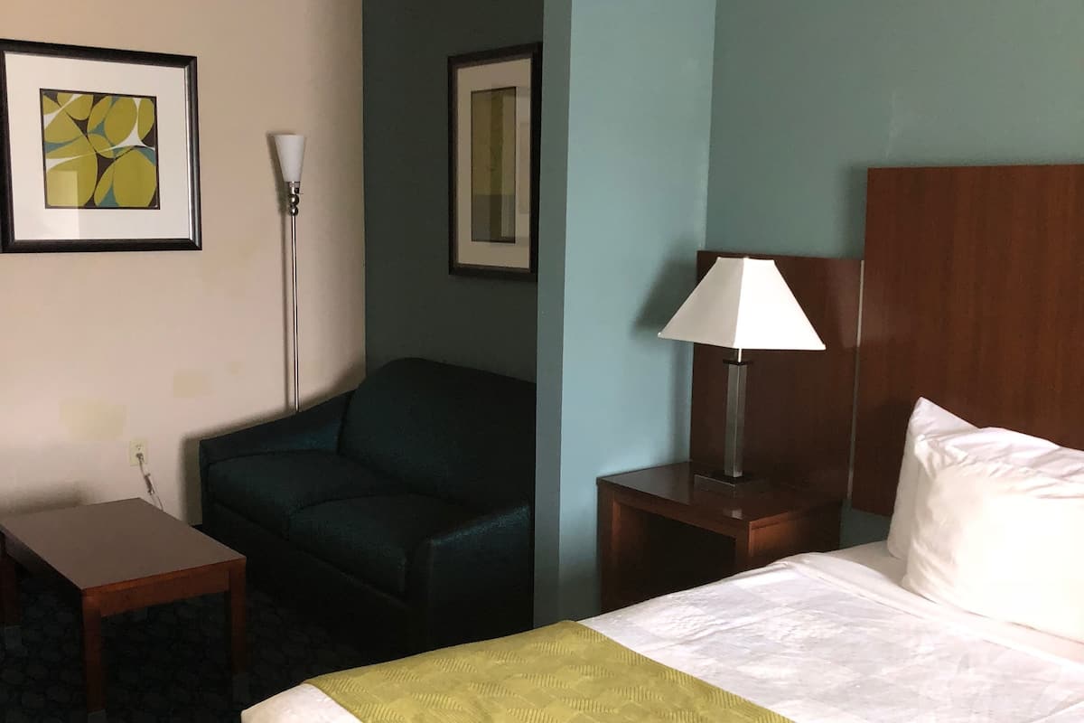 A hotel room with a bed, a desk, a chair, a lamp, and two framed pictures on the wall.