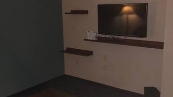 A room with a television mounted on the wall, a wooden bench, and a small trash bin.