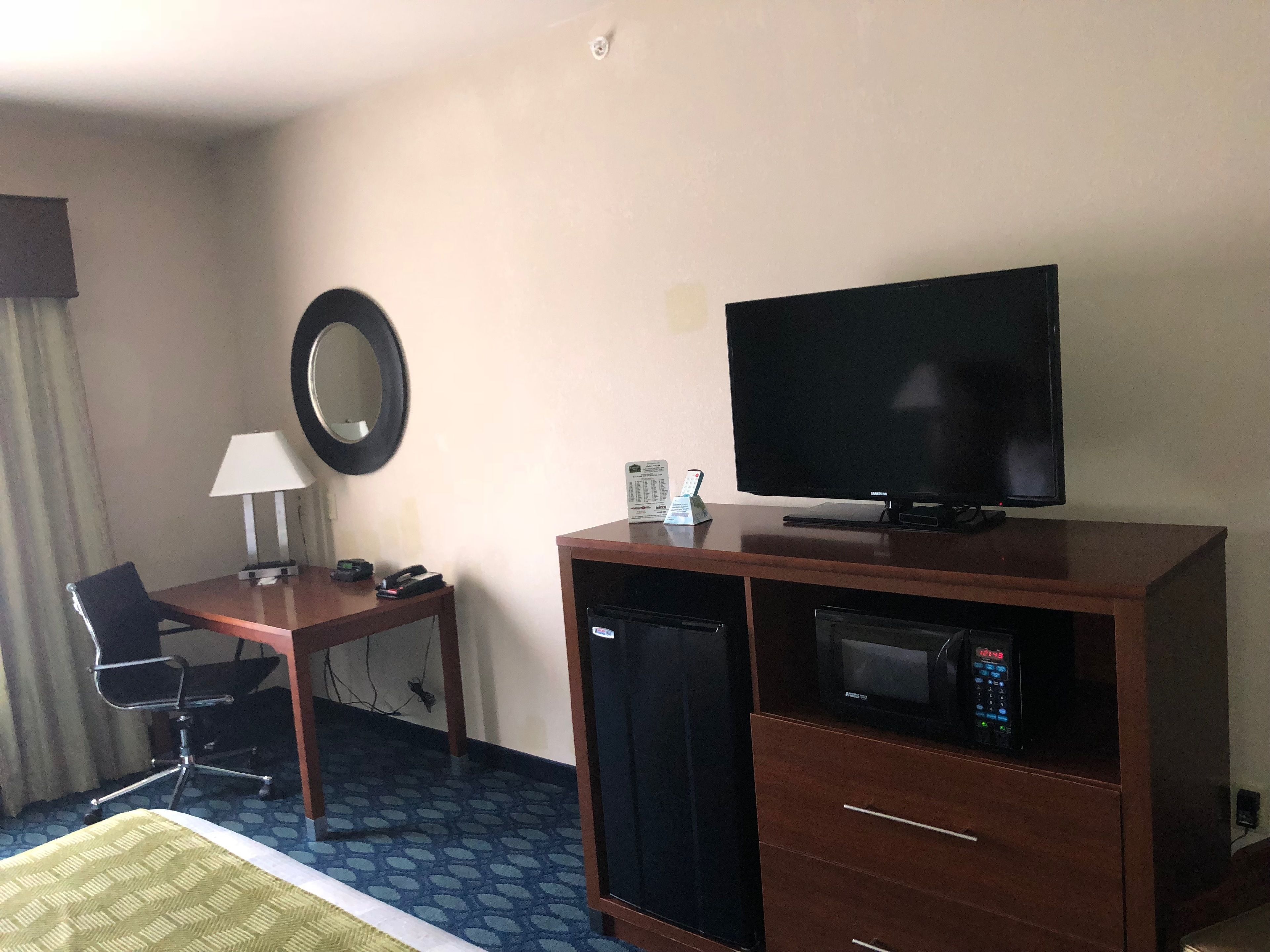 A hotel room with a bed, a desk with a lamp, a television, a microwave, and a chair.