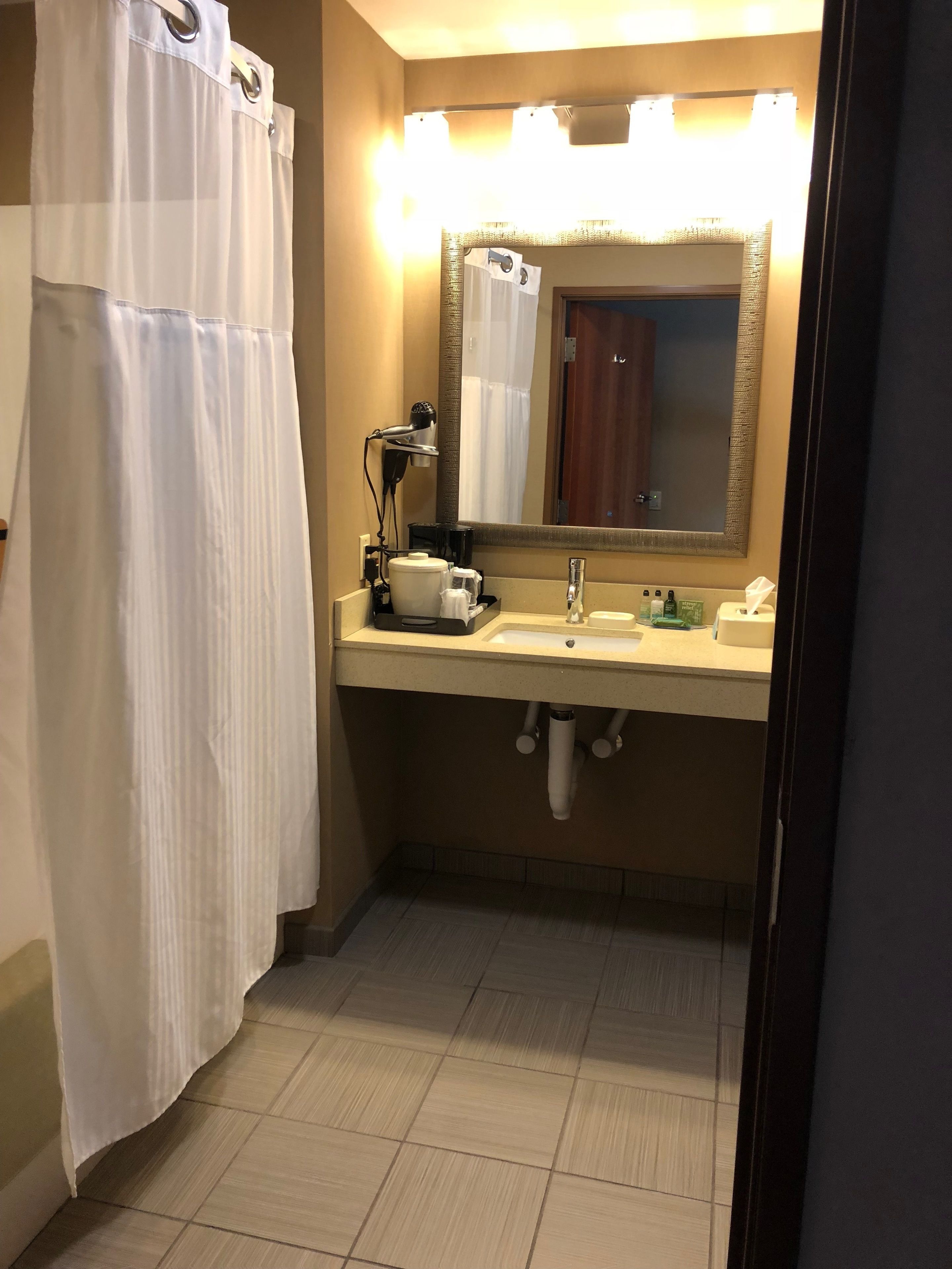 Casa de banho com cortina de chuveiro, espelho, lavatório, secador de cabelo e porta-toalhas.