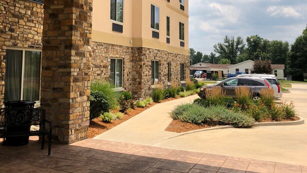 Un edificio con fachada de piedra y múltiples ventanas, un patio cubierto con un banco y un estacionamiento con varios coches.