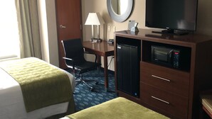 Habitación de hotel con dos camas, un escritorio con lámpara, televisión, minibar y un espejo en la pared.