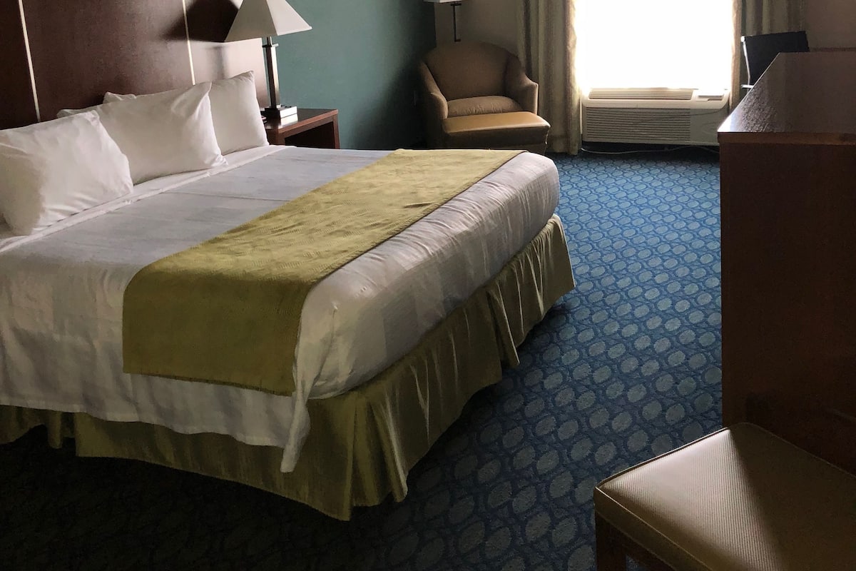 A hotel room with a large bed, a chair, a desk, and a window with curtains.