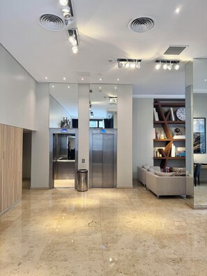 A modern lobby with a marble floor, a reception desk, a staircase, and a bookshelf with a clock. - Carles Hotel Buenos Aires (Buenos Aires)