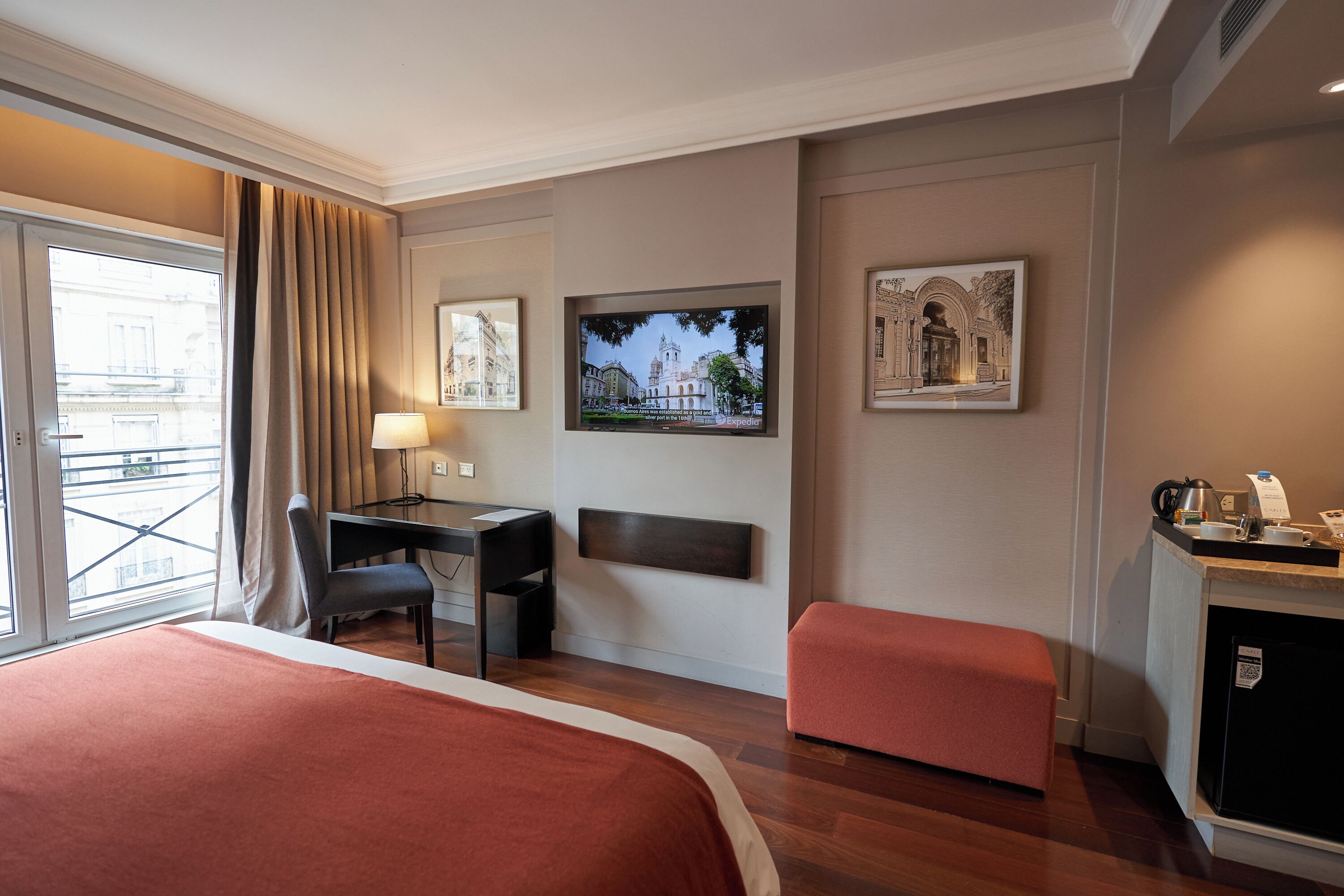 A hotel room with a bed, a desk, a chair, a television, and a small kitchenette.
