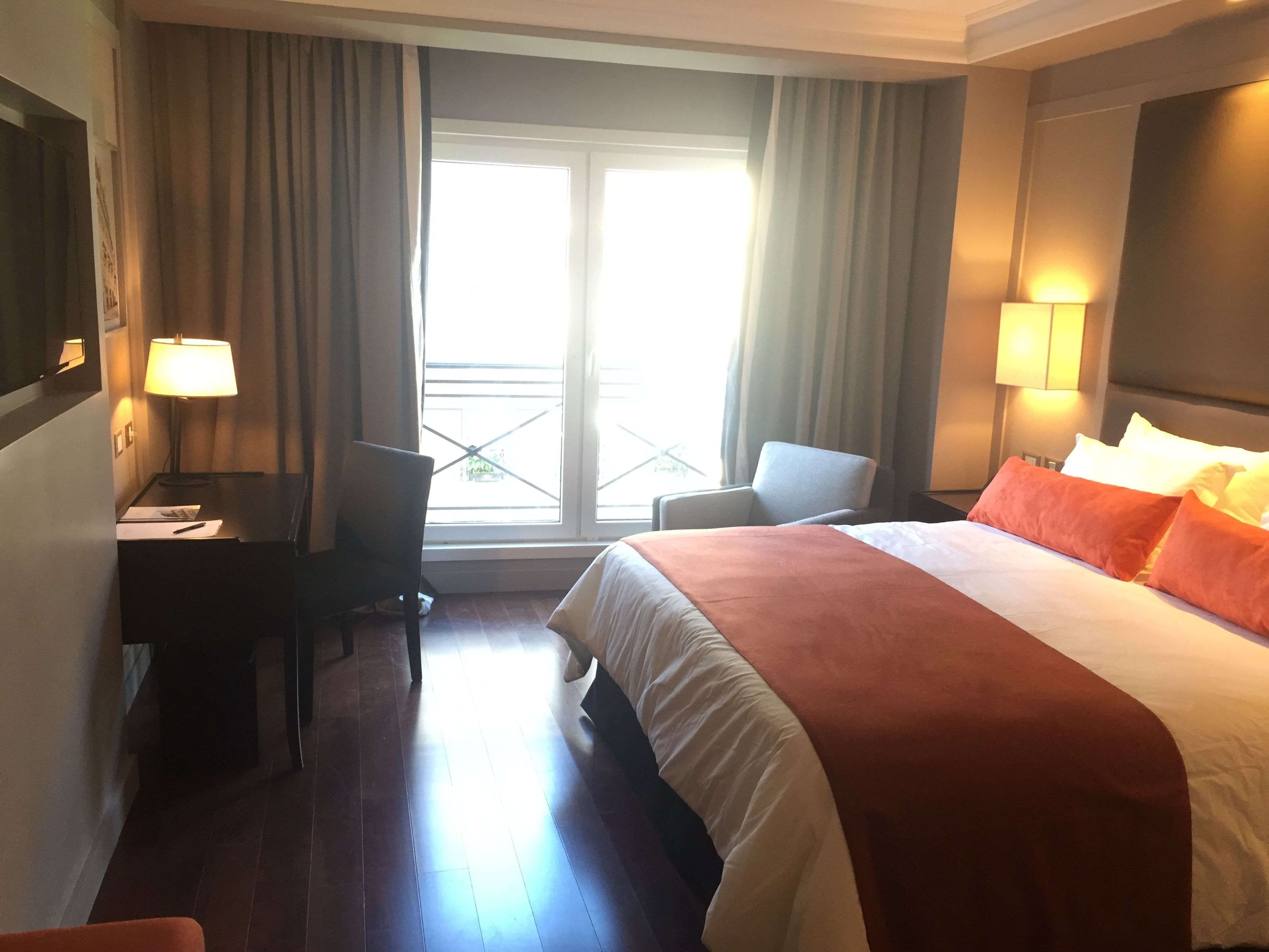 Una habitación de hotel con cama, escritorio, silla y ventana con cortinas.
