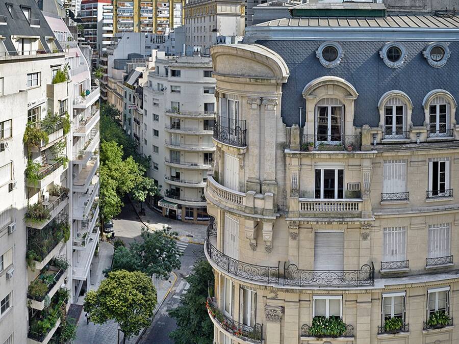 A multi-story building with balconies, a street in front, and other buildings in the background.